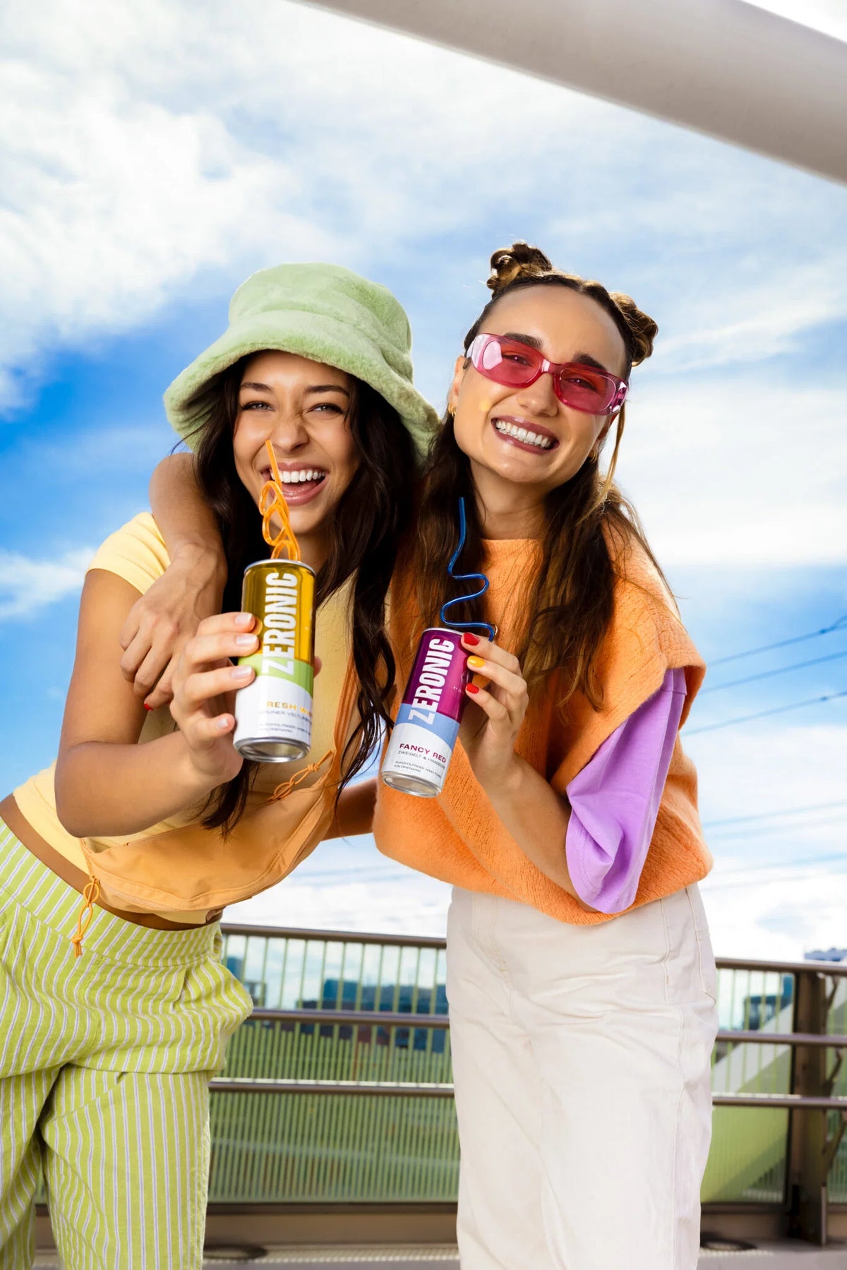 Two friends laughing outdoors, holding cans of Zeronic Fresh White and Zeronic Fancy Red